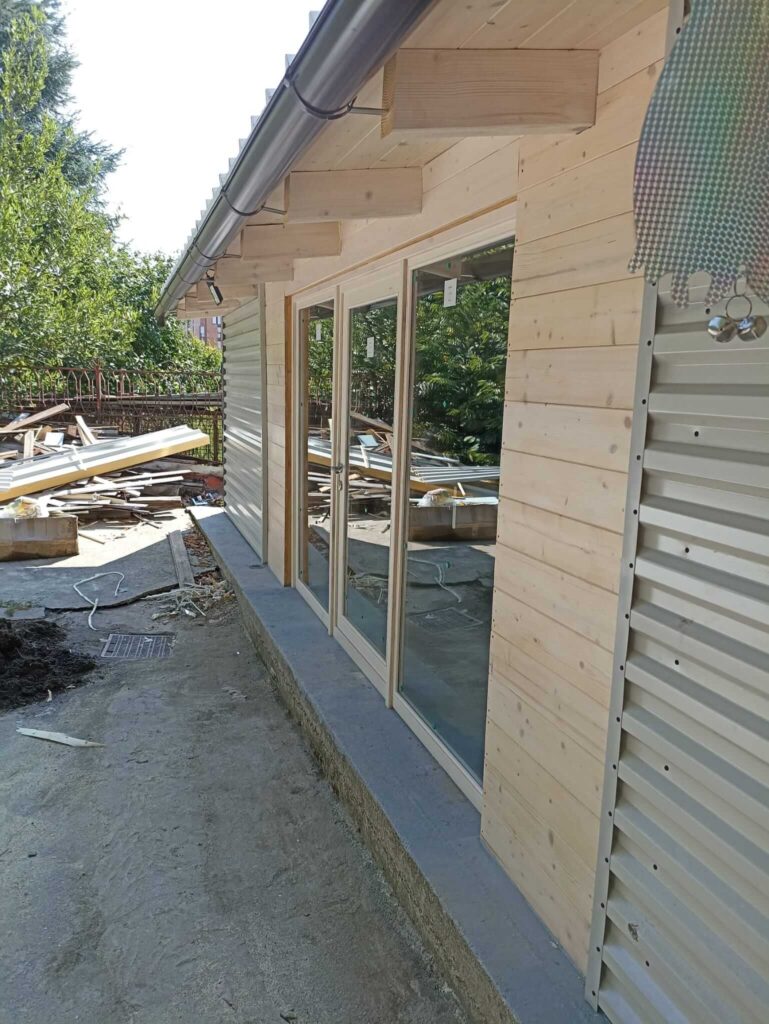 Vista laterale della casetta da giardino in legno con porte scorrevoli vetrate installate